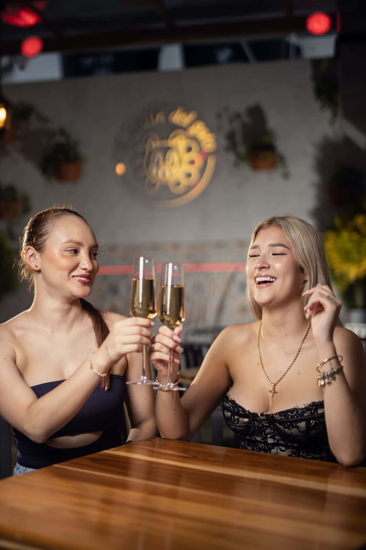 Two friends toast at a patio table, under the cat sign
