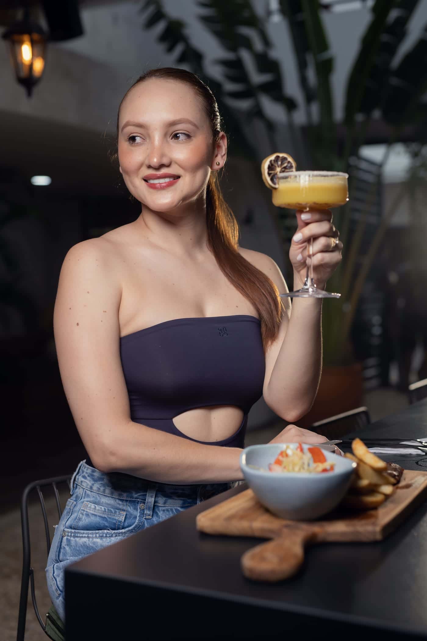 A guest raises a cocktail at her table, with a dish served