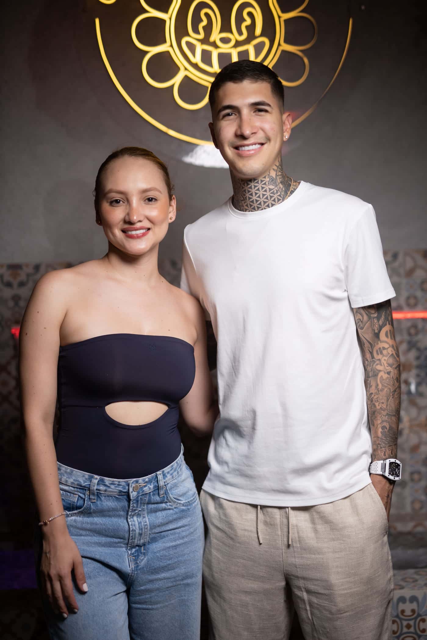 A couple poses in front of the lit cat logo