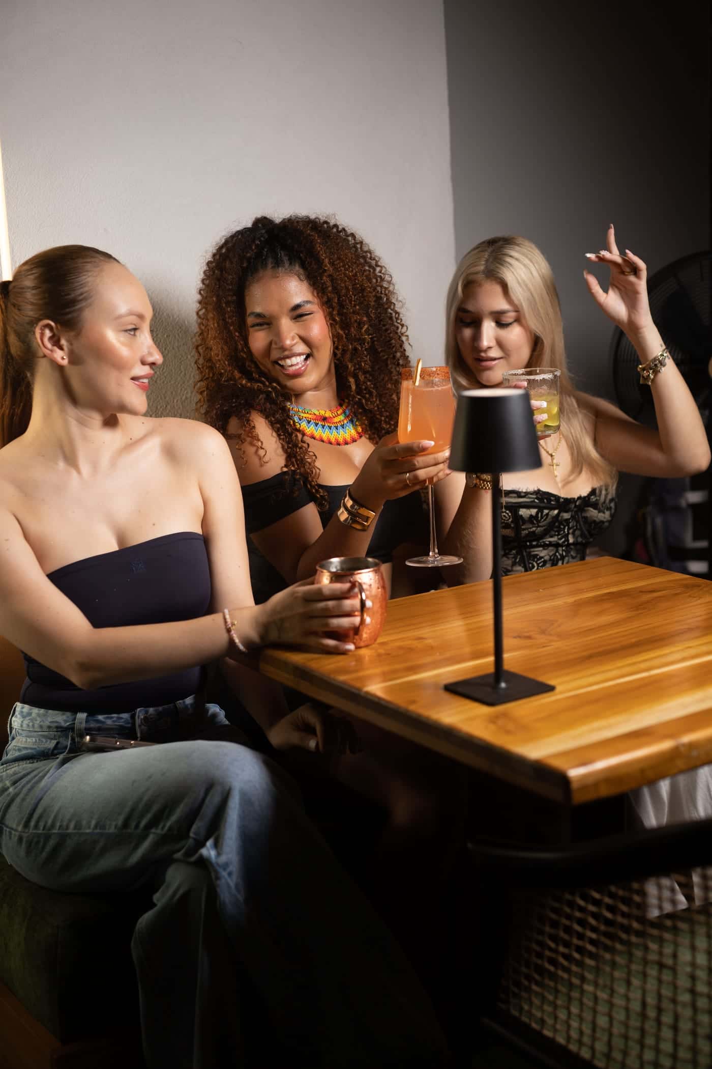 Three friends laugh at a garden table with their cocktails