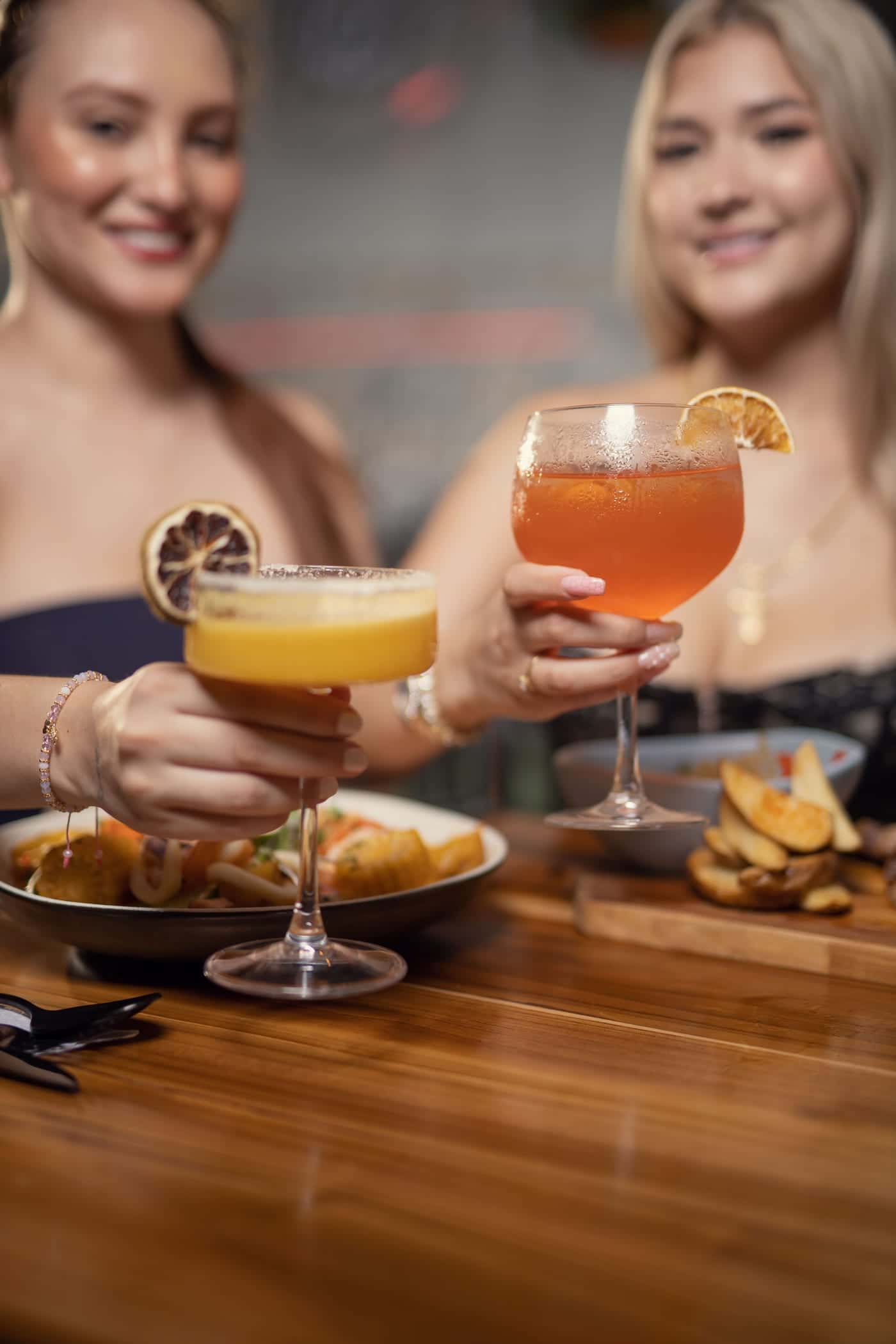 Two cocktail glasses clink in a toast over the table