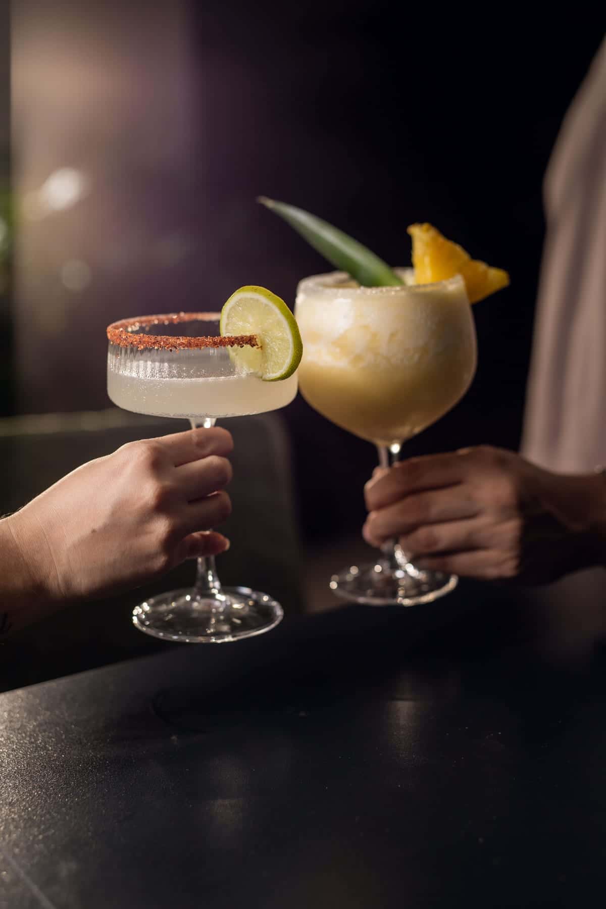 Two hands toast with a margarita and a piña colada at the bar