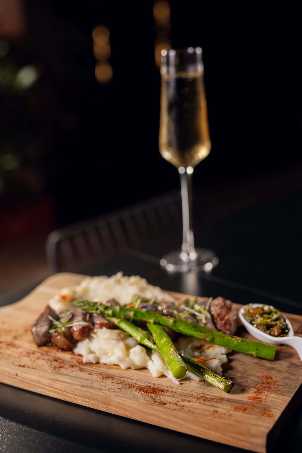 A New York steak with asparagus on a wooden board and a glass of sparkling wine, at a patio table