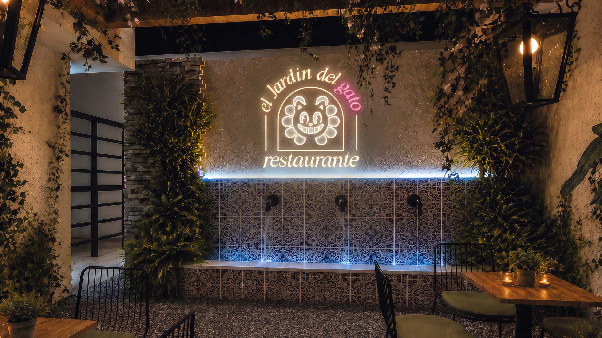 El letrero de neón de El Jardín del Gato sobre los azulejos y la fuente del patio